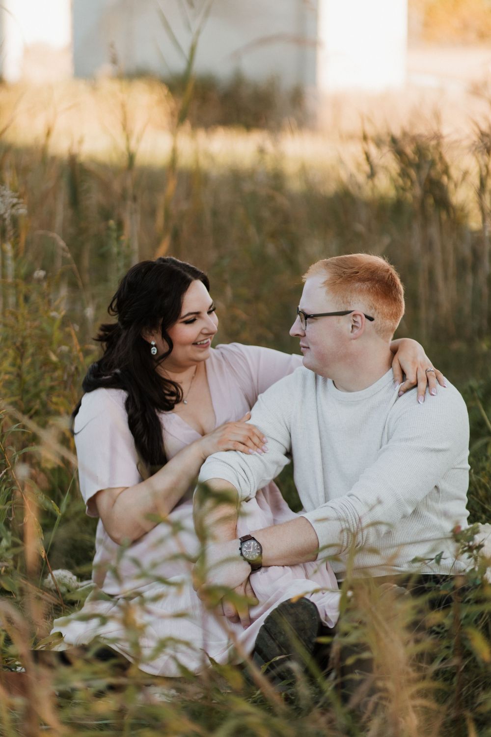 Happy couple sitting together in tall golden grass during a warm sunset session.