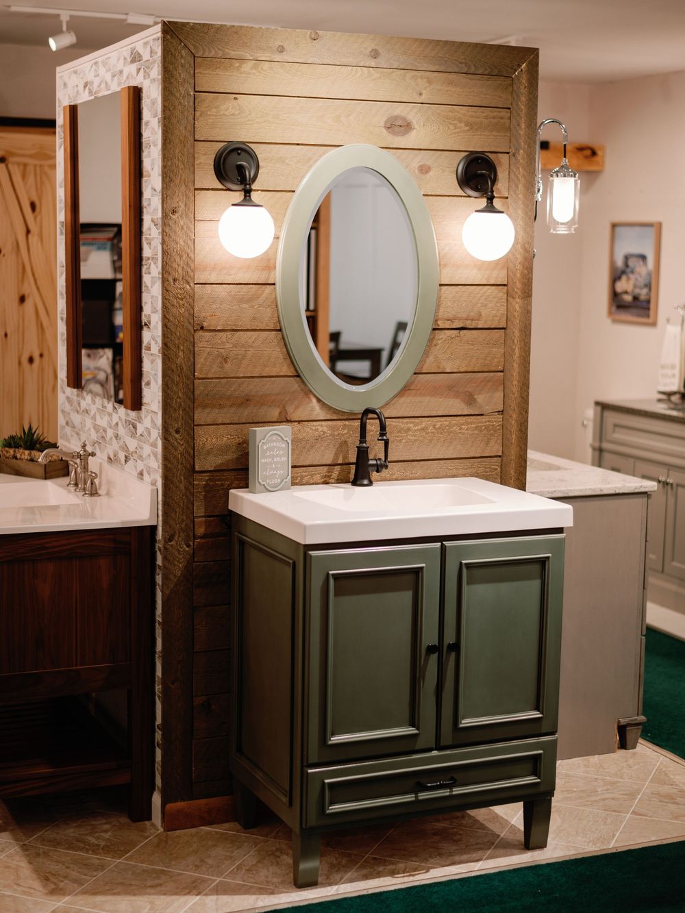 A rustic bathroom renovation featuring wood plank walls, green vanity cabinets, and contemporary lighting fixtures.