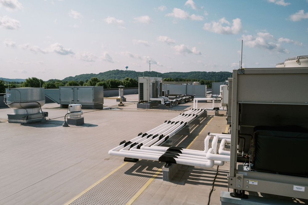 Aerial view of an airport terminal rooftop with HVAC equipment and mechanical systems against a blue sky with clouds.