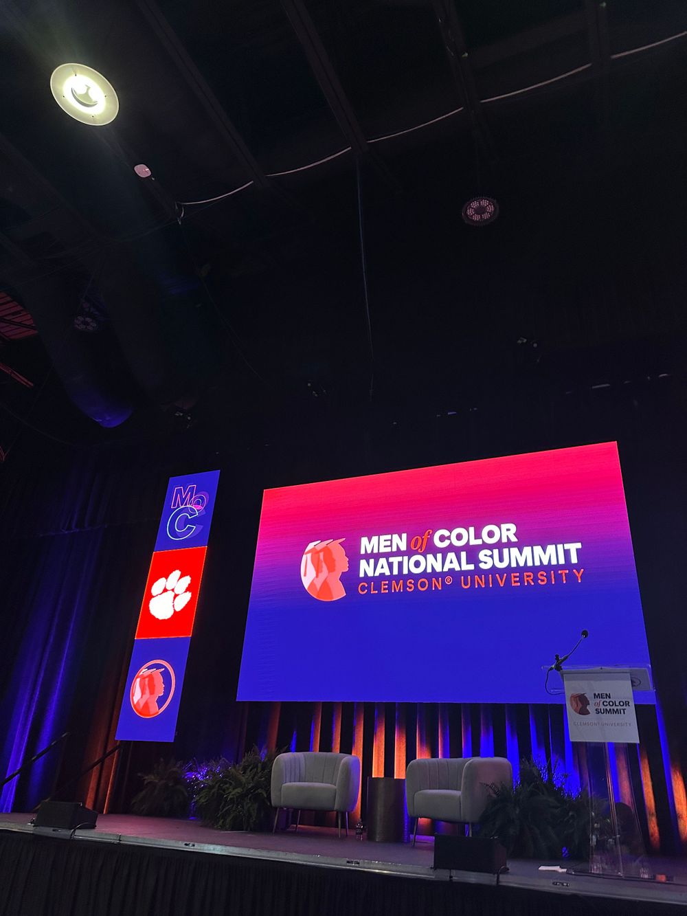 Conference stage setup with Men of Color National Summit branding displayed on large screen.