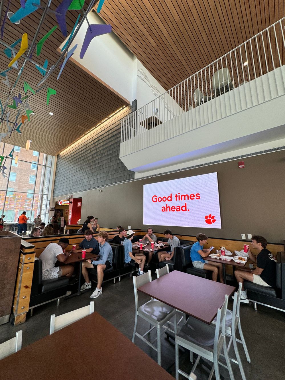 Modern campus dining area with wooden ceiling, digital display showing 'Good times ahead' message.