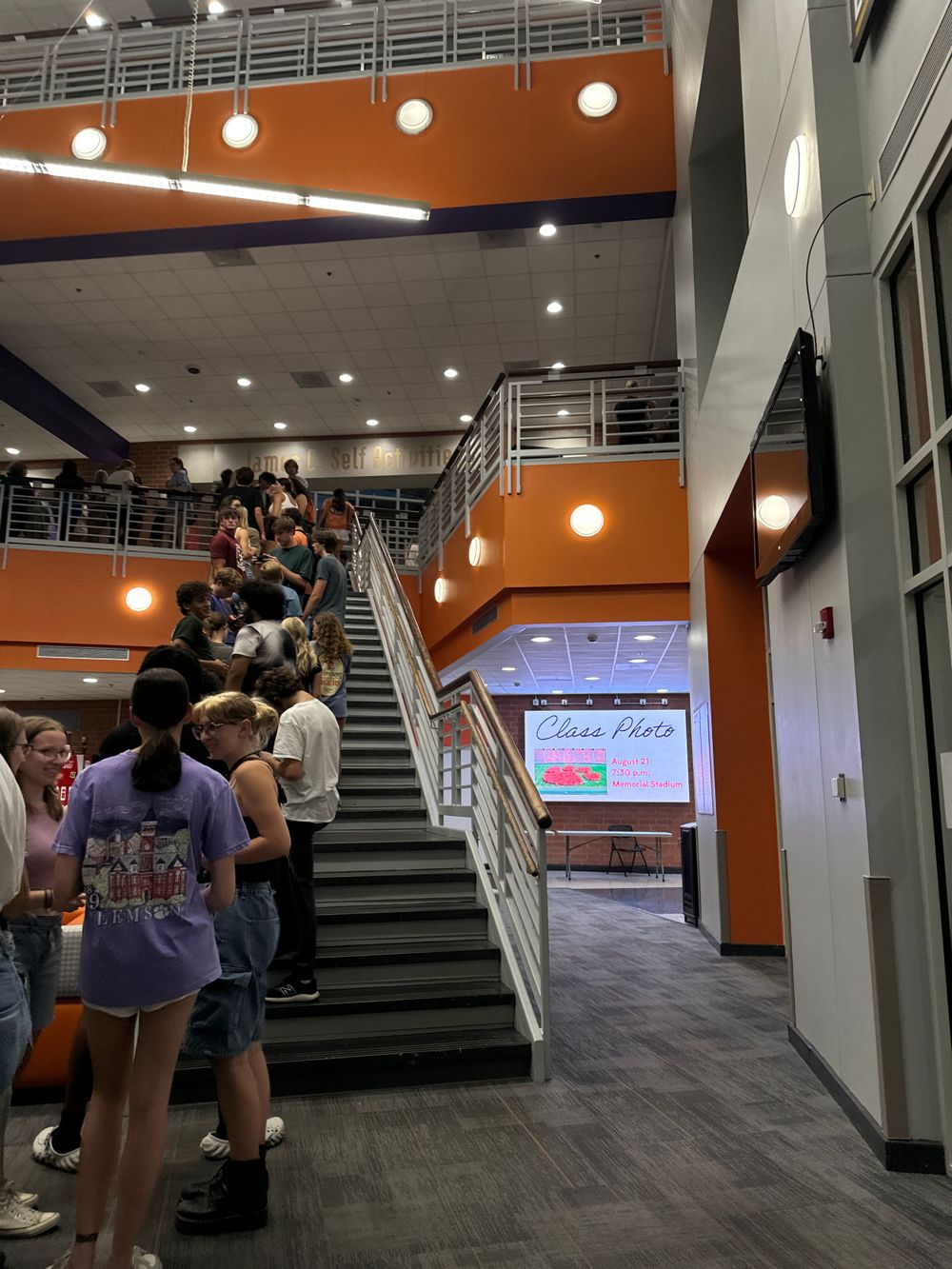 Modern university building interior with orange walls and stairs filled with students.