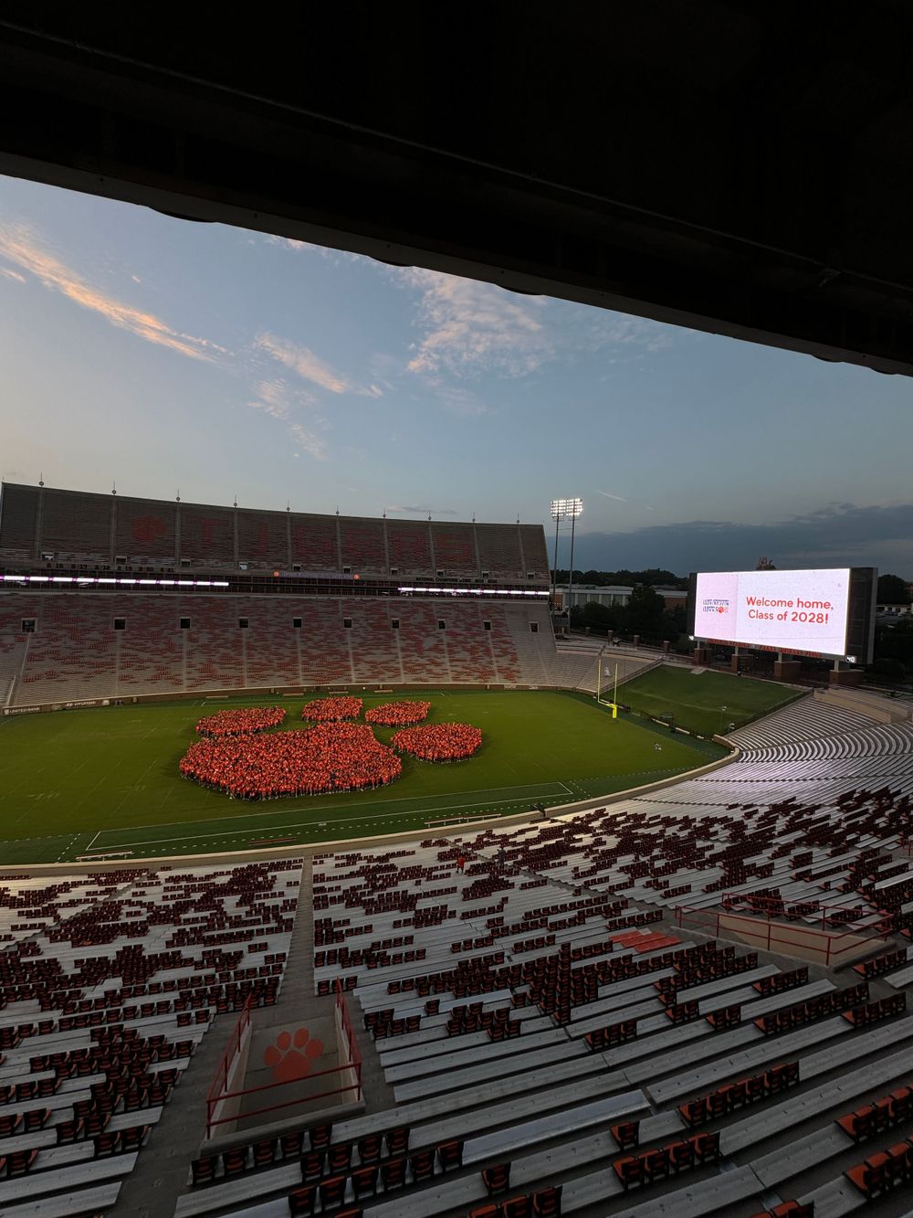 Aerial view of students forming giant paw print formation on Clemson football field at sunset.