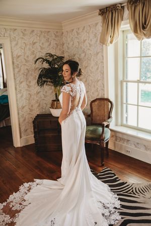 Bride in elegant white lace-back wedding gown with train poses in a beautifully decorated room with hardwood floors.