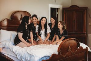 Group sitting together on antique bed sharing laughs during wedding preparations.