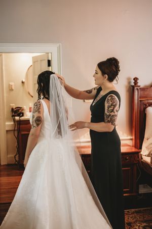 Helper adjusting bridal veil on bride wearing traditional white wedding gown.