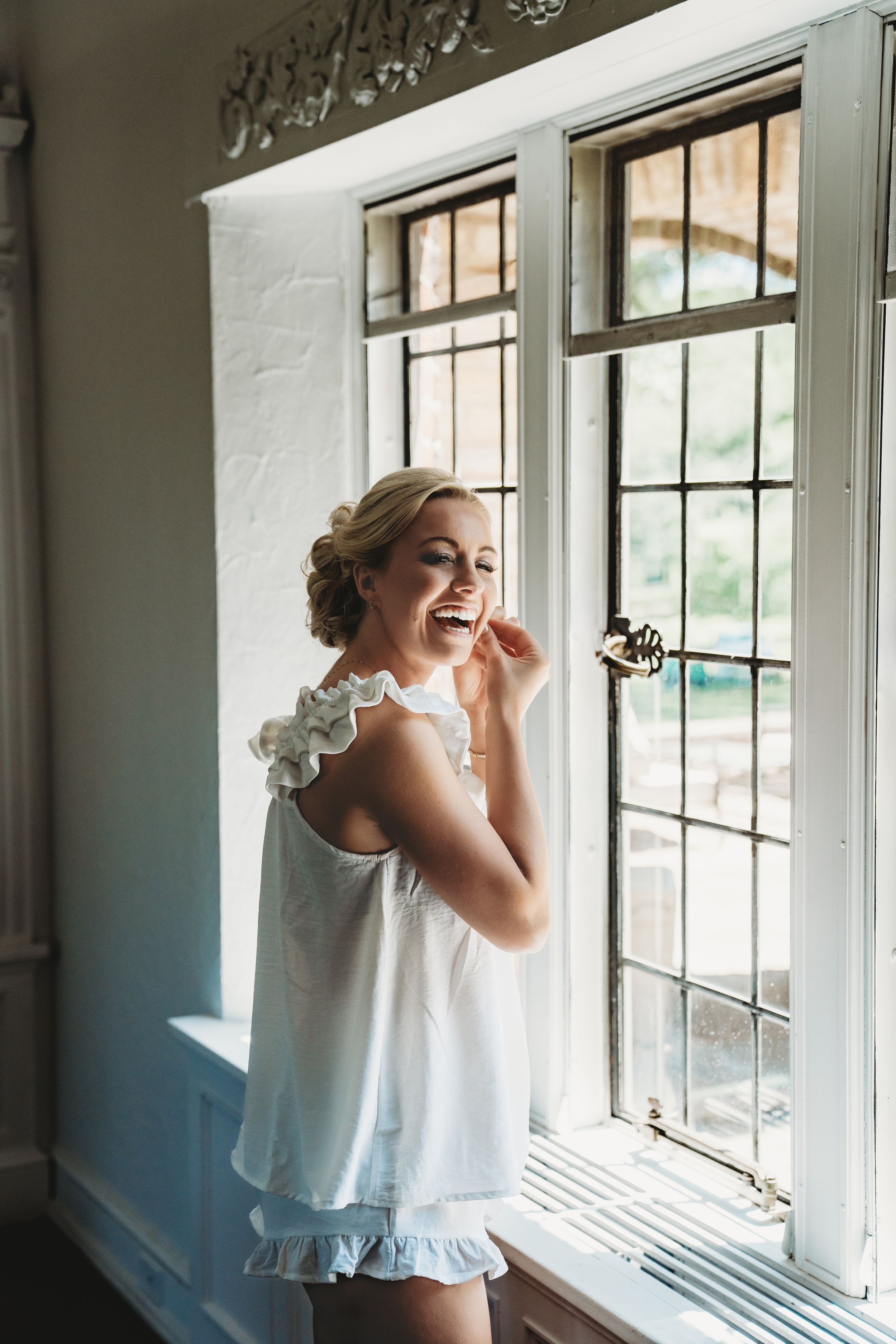 A joyful moment captured by a window as morning light streams in, highlighting a white ruffled nightgown.