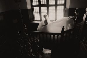 A dramatic black and white photograph showing silhouettes against bright windows in a moody interior space.