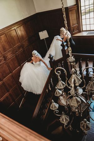 Two wedding dresses displayed on a grand wooden staircase with an ornate chandelier hanging above.