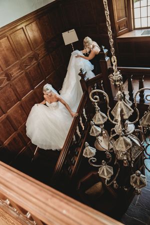 A dramatic wedding photo on a staircase with a beautiful chandelier featuring a flowing white dress and dark wood paneling.