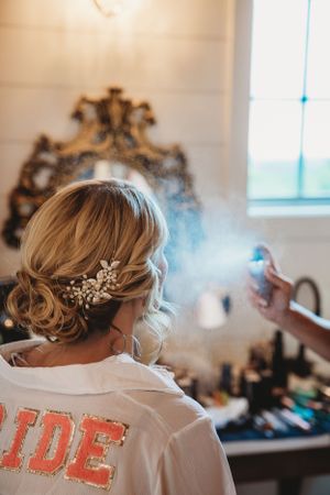 Bride in custom robe gets final touches on her braided wedding hairstyle.