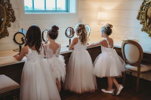 Flower girls in white tulle dresses gather during wedding preparations.