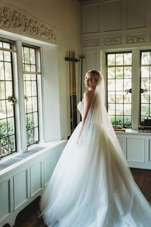Wedding gown with dramatic ballgown silhouette and cathedral veil photographed in a bright interior space.