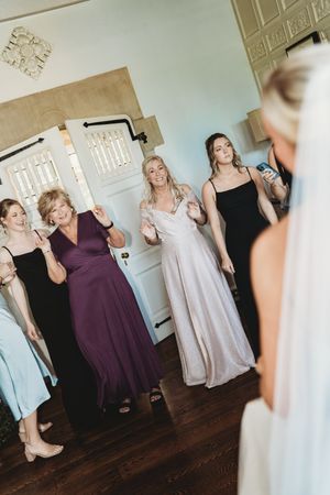 Wedding party members in purple and black dresses react with joy during a special moment.