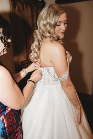 Bride in a backless beaded wedding gown getting dressed with help from a bridesmaid.