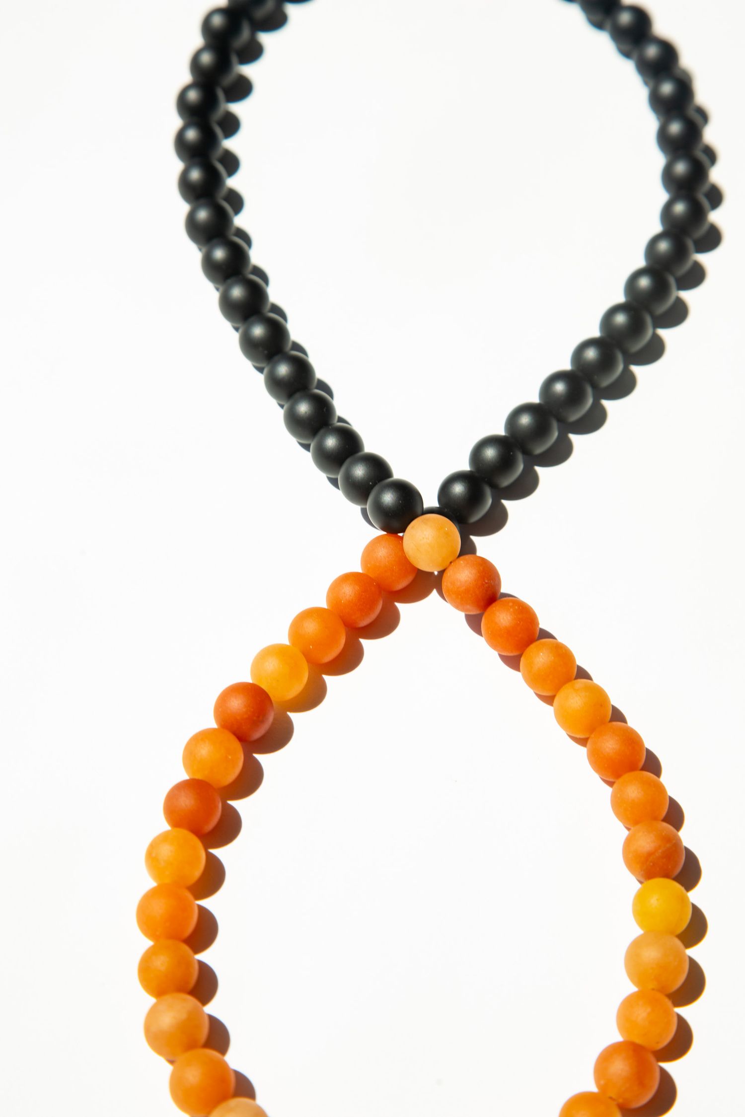 Black and orange beaded necklaces arranged in curved patterns on white background.