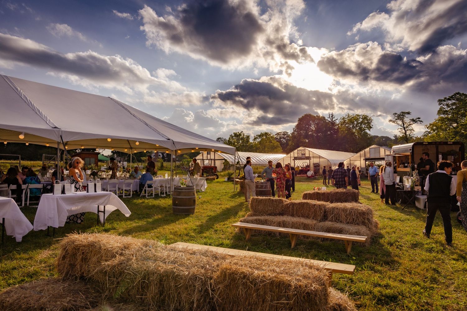 Wedding tents and reception setup on a hilltop during golden hour with dramatic clouds.