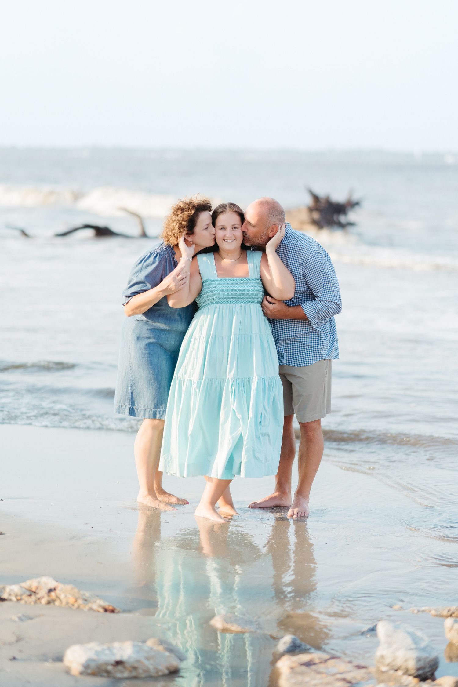 Parents kissing their daughter’s cheeks in the shallow surf during a family portrait session on Jekyll Island.