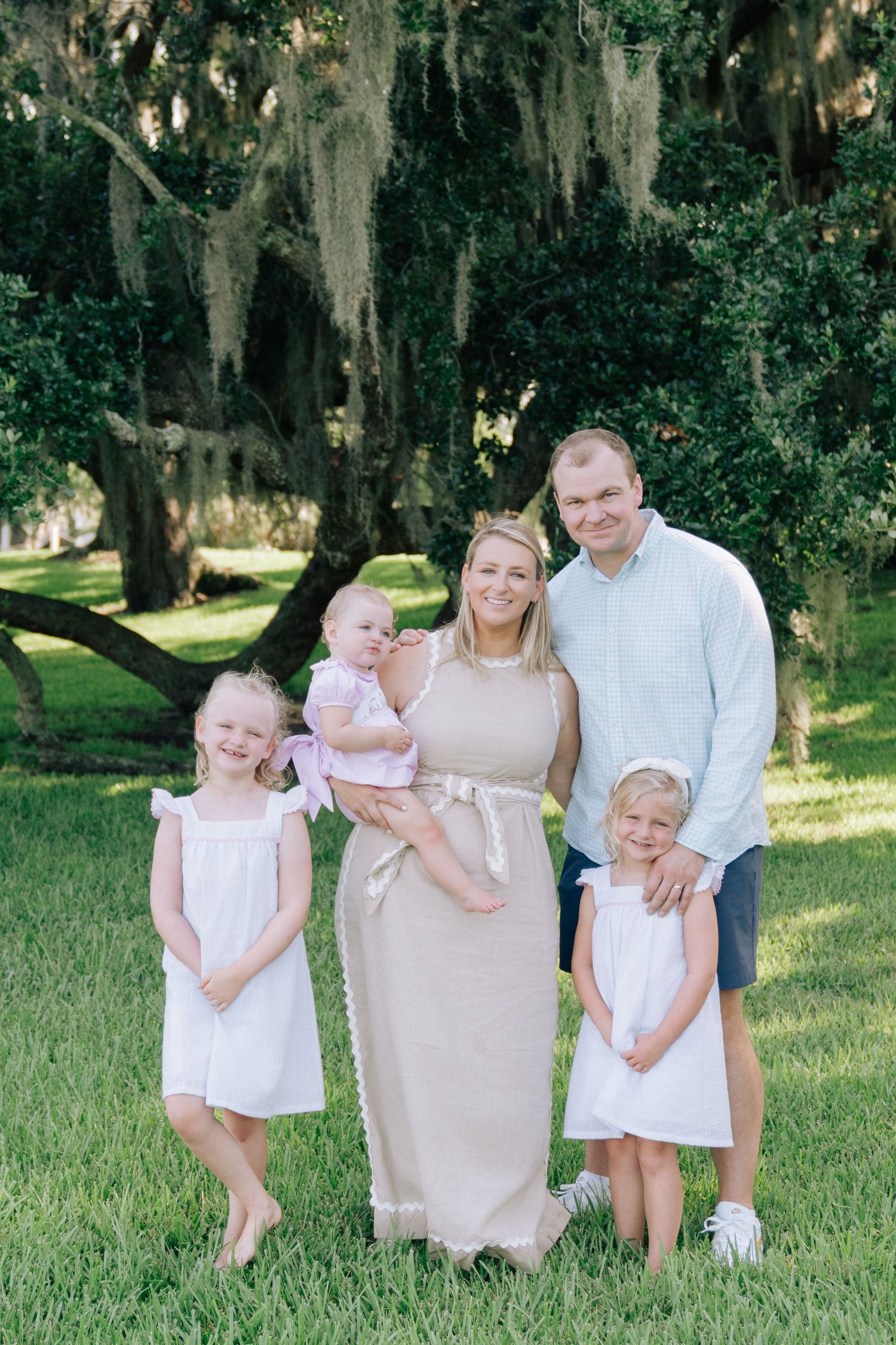 Parents and three young children posing beneath oak trees during a family portrait session.
