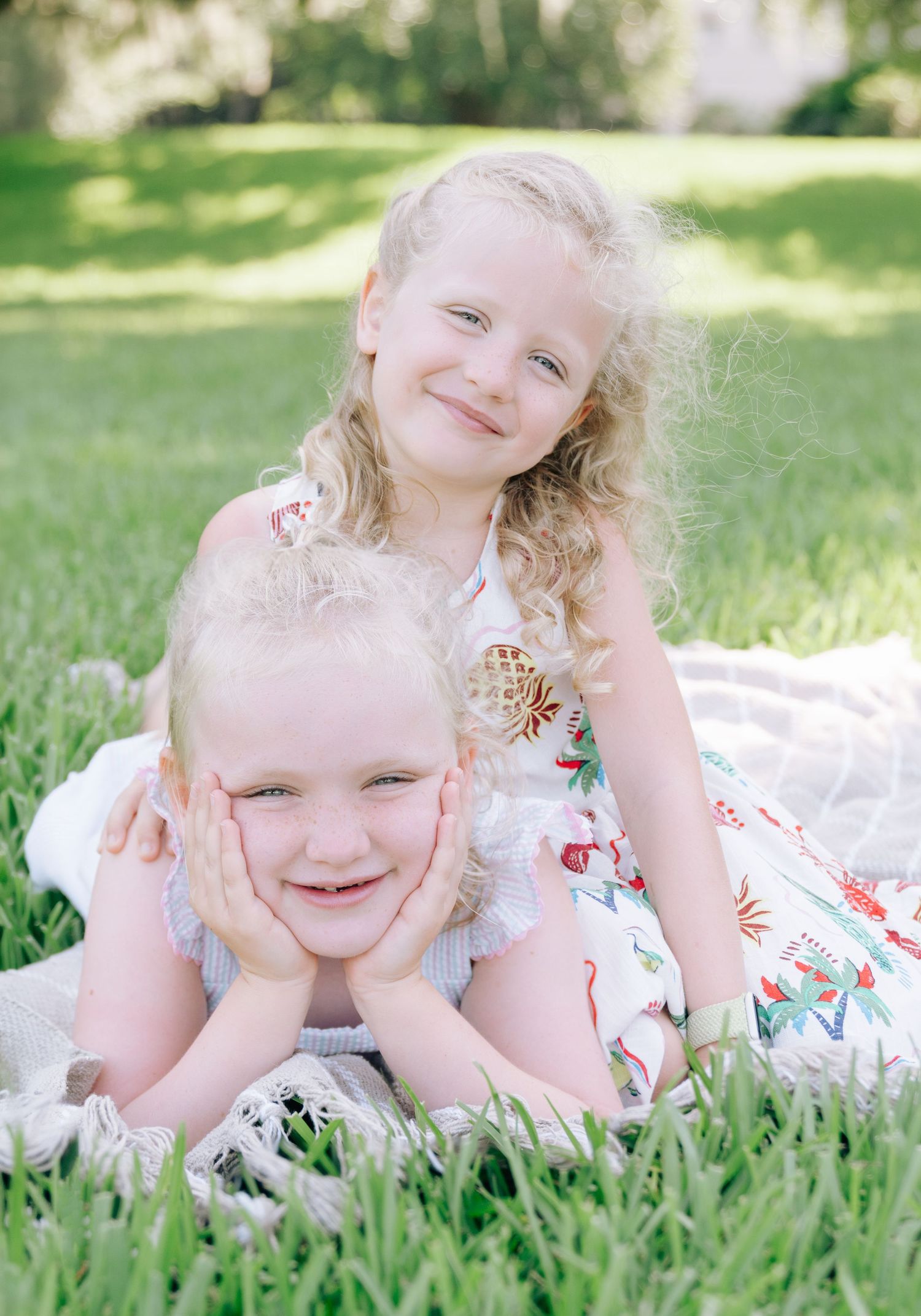 Two smiling girls in floral dresses on a picnic blanket during an outdoor family photography session in Fernandina Beach and Amelia Island