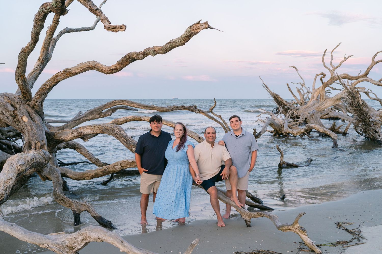 Family of four posing among driftwood beside the ocean during an evening portrait session on Jekyll Island, Georgia.