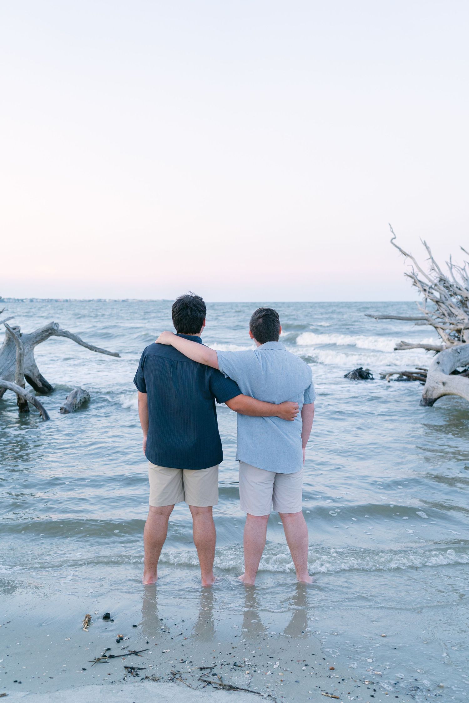 Two teenage brothers standing arm in arm at the ocean’s edge during a family portrait session on Driftwood Beach, Jekyll Island.