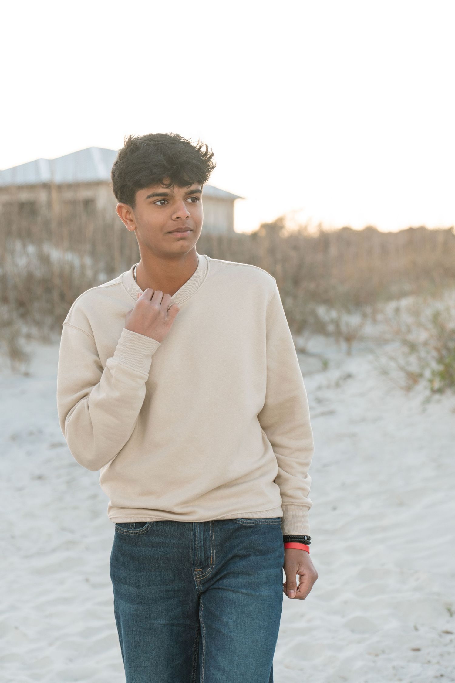 Teenager in a cream sweater standing beside beach dunes during an individual portrait at sunset.