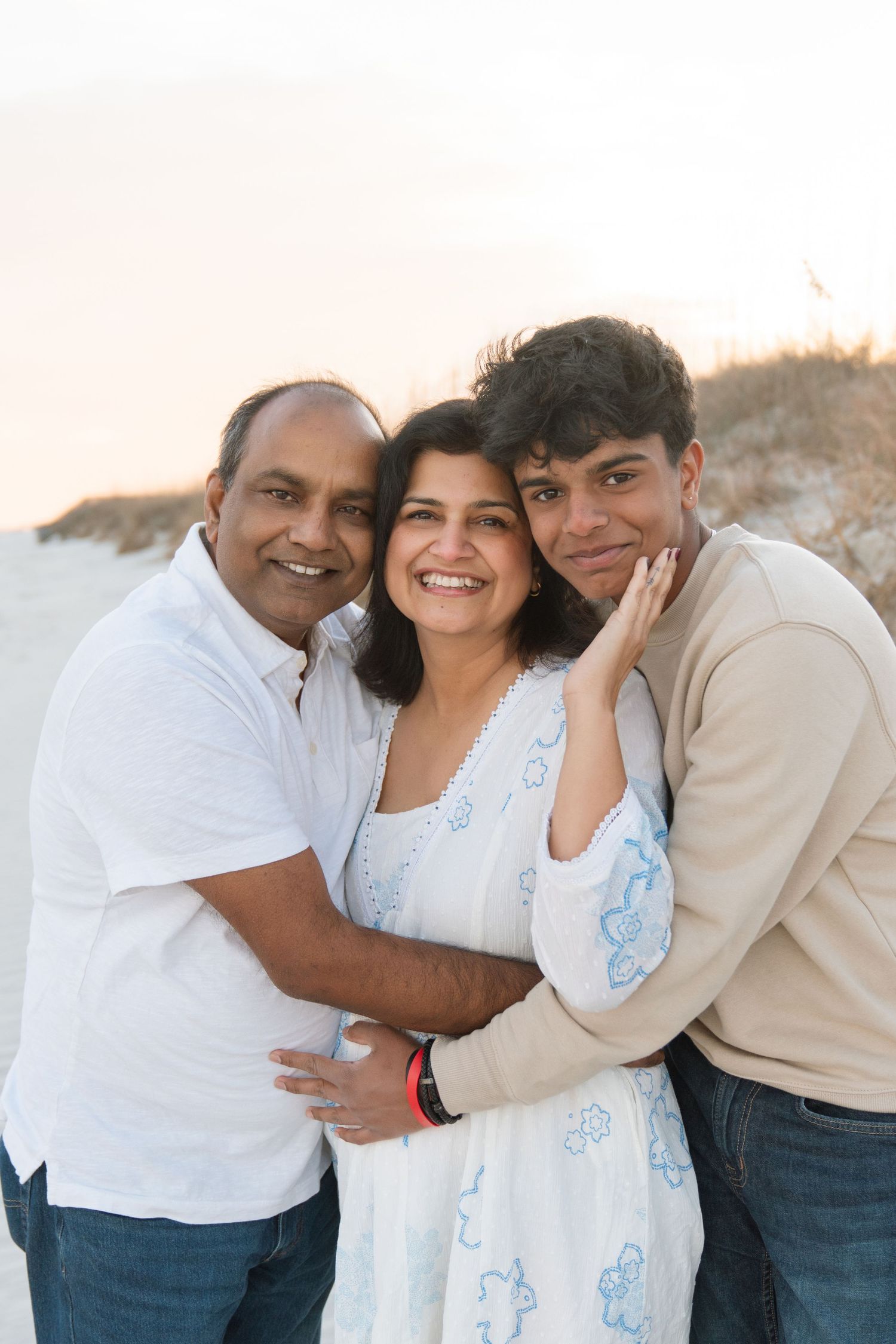 Family of three embracing beside coastal sand dunes during a sunset beach portrait session in the winter near North Jacksonville