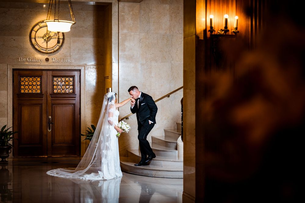 Bride and groom share a romantic moment on grand marble staircase in elegant wedding venue lobby.