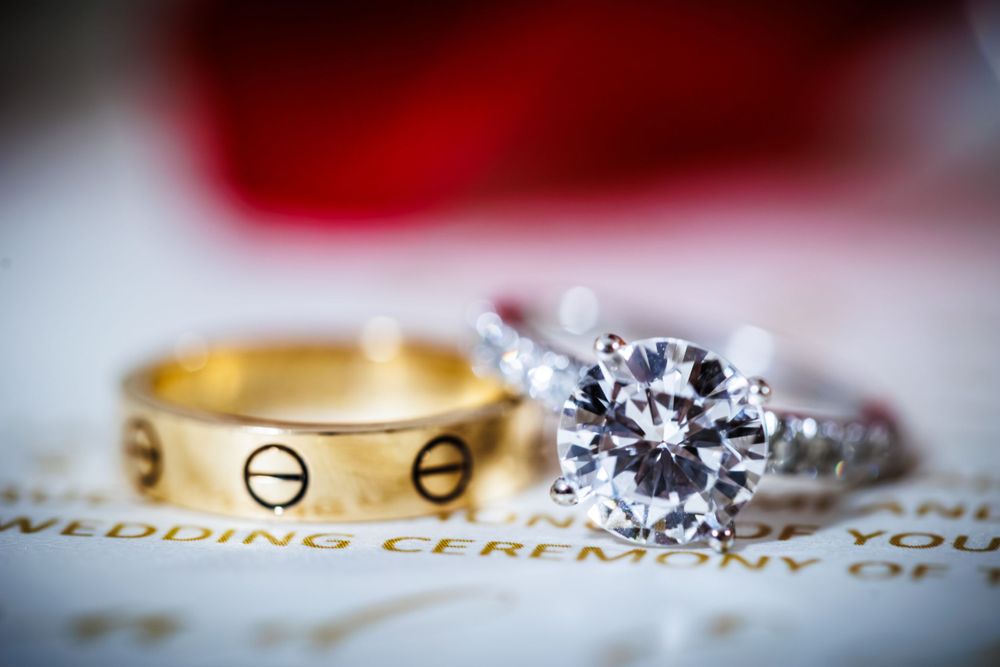 Two wedding rings on paper, one gold band with screw designs and one silver with large diamond solitaire.