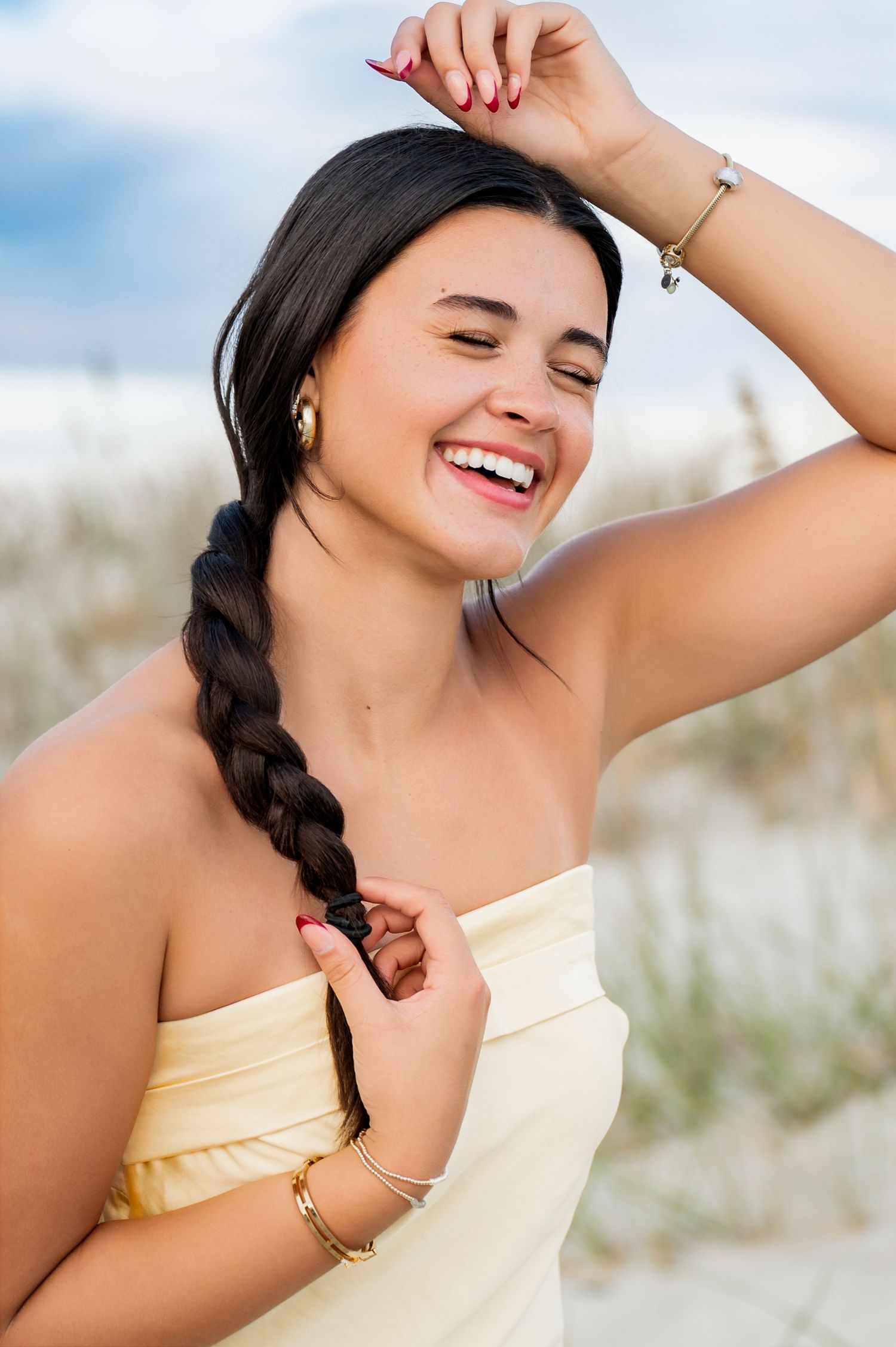A person in a cream dress shows joyful expressions while posing on the beach.