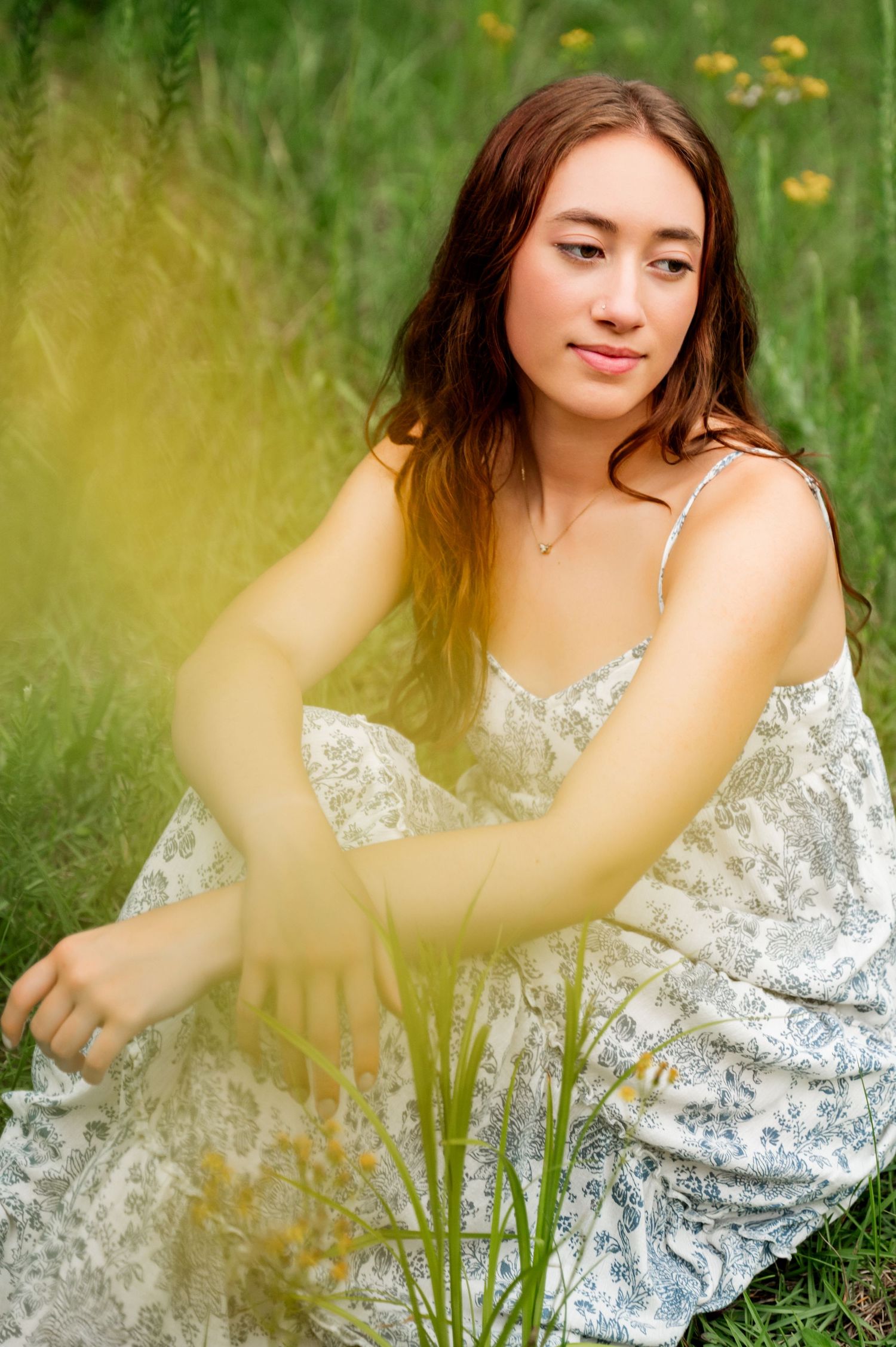 Figure in white floral top poses gracefully among tall grass and yellow wildflowers.