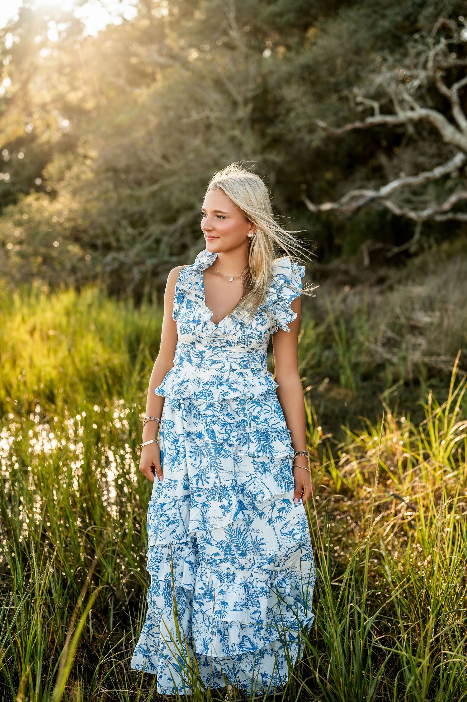 Person in blue and white floral dress twirls in golden sunset light among tall grass.
