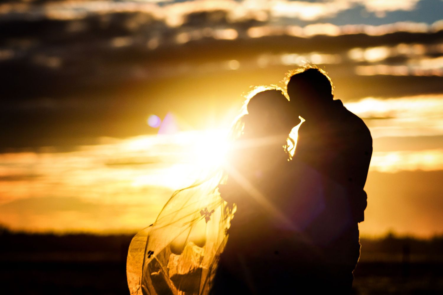 Silhouetted figures embrace during golden sunset with dramatic sky.