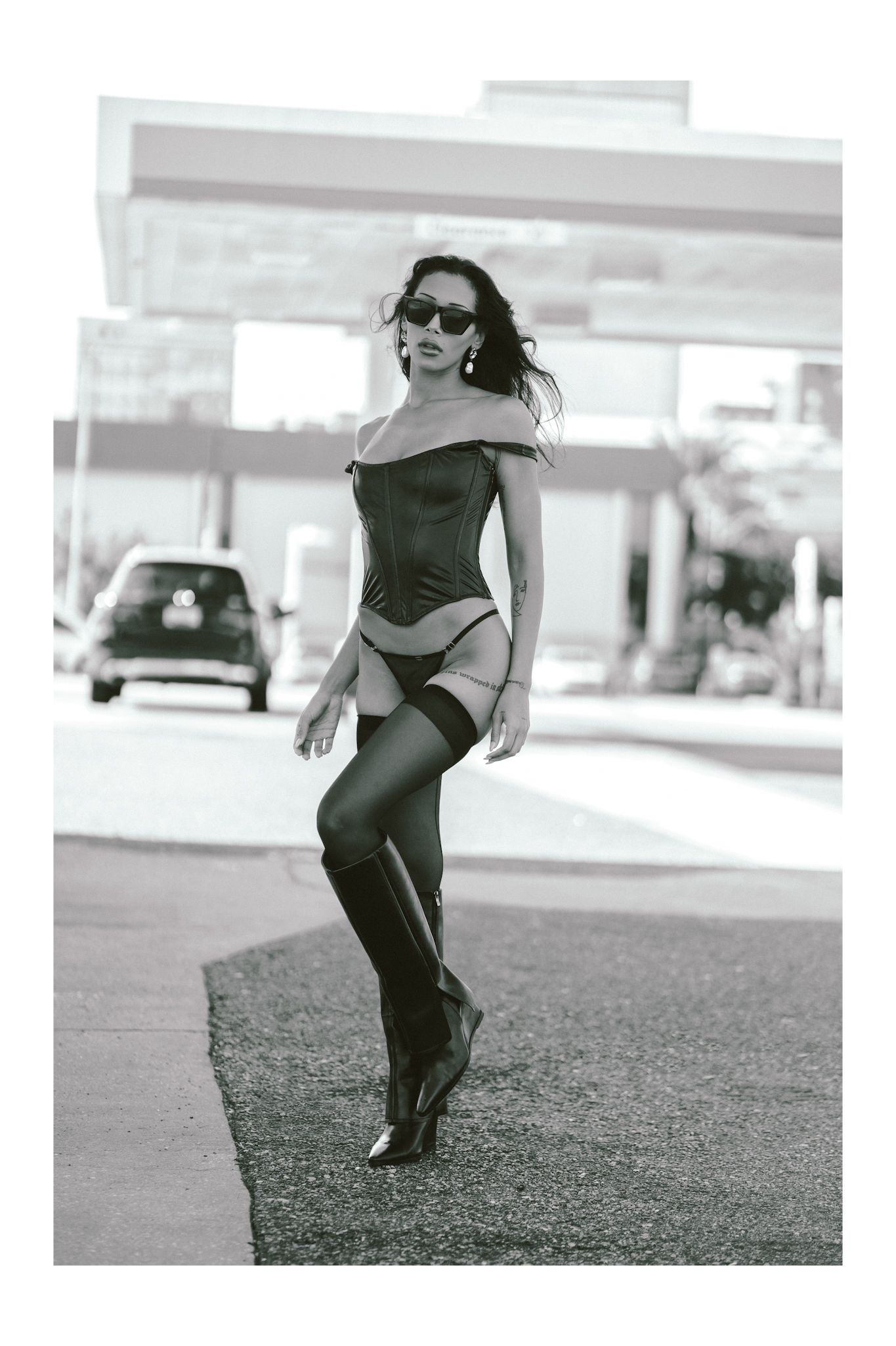 Black and white fashion photo showing model in corset and boots on street.