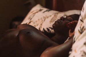 Artistic boudoir photo showing silhouette resting on patterned bedding in warm lighting.