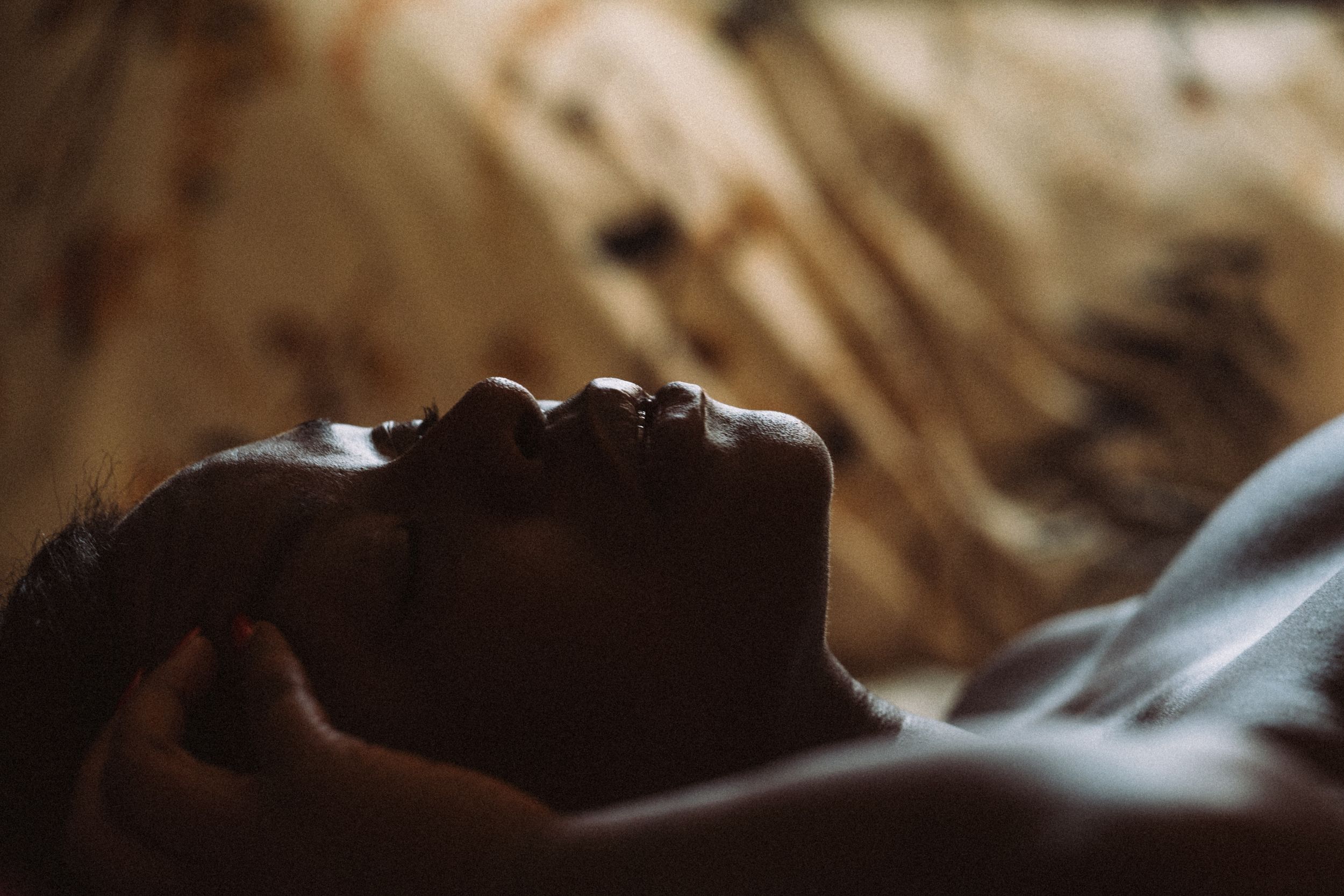 A person lying down in soft lighting creates a dramatic silhouetted profile against a warm brown background.