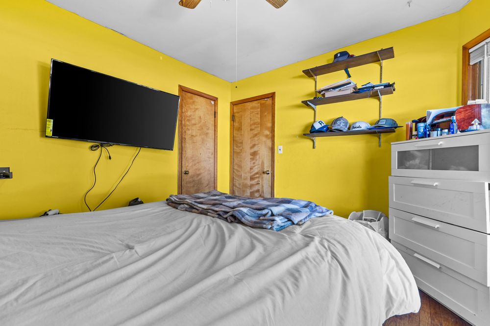 Yellow bedroom with wall-mounted TV, ceiling fan, and white dresser.