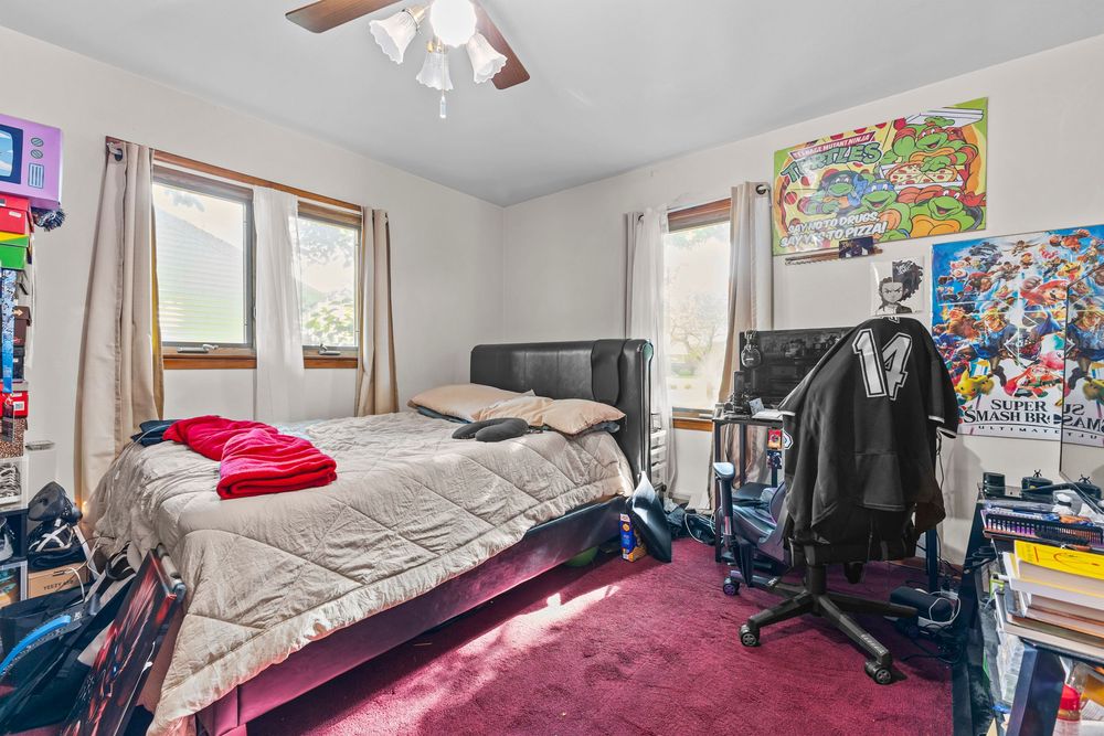 Carpeted bedroom with two windows, ceiling fan, and red area rug.
