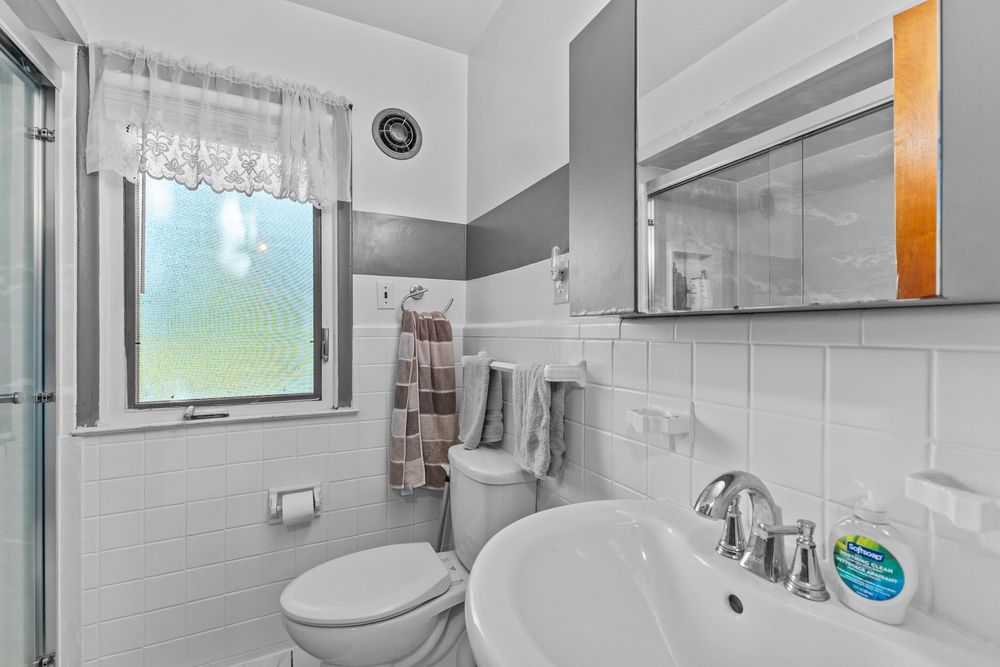 White tiled bathroom with pedestal sink, toilet, and medicine cabinet.