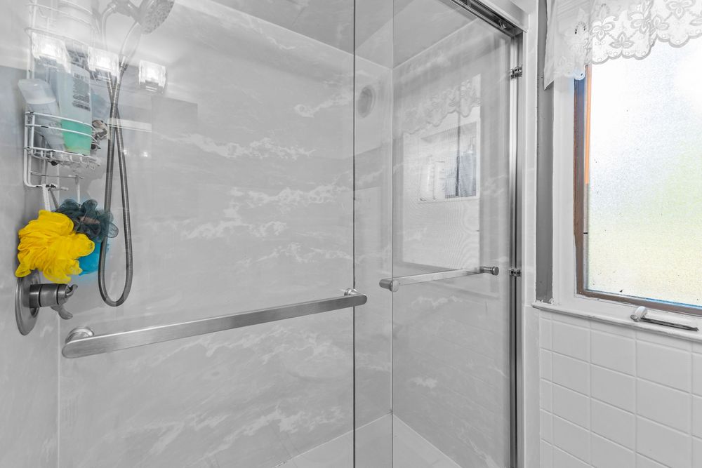 Modern glass-enclosed shower with marble-style tiles and handheld showerhead.