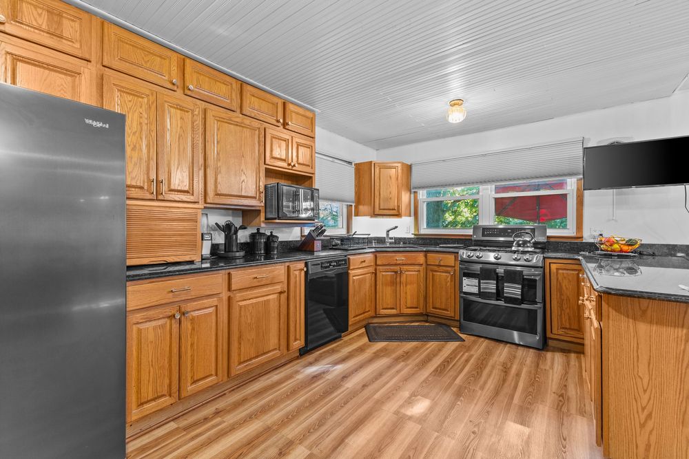 Spacious kitchen with honey oak cabinets, black appliances, dark countertops, and hardwood floors in a bright open layout.