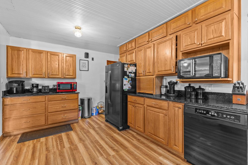 Oak kitchen cabinetry with dark countertops, black refrigerator, and microwave on light hardwood flooring.