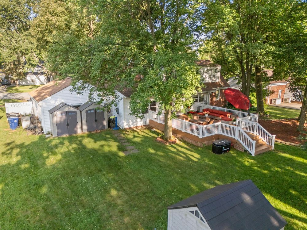 Aerial view of backyard with large deck, storage shed, lush green lawn, and mature trees.