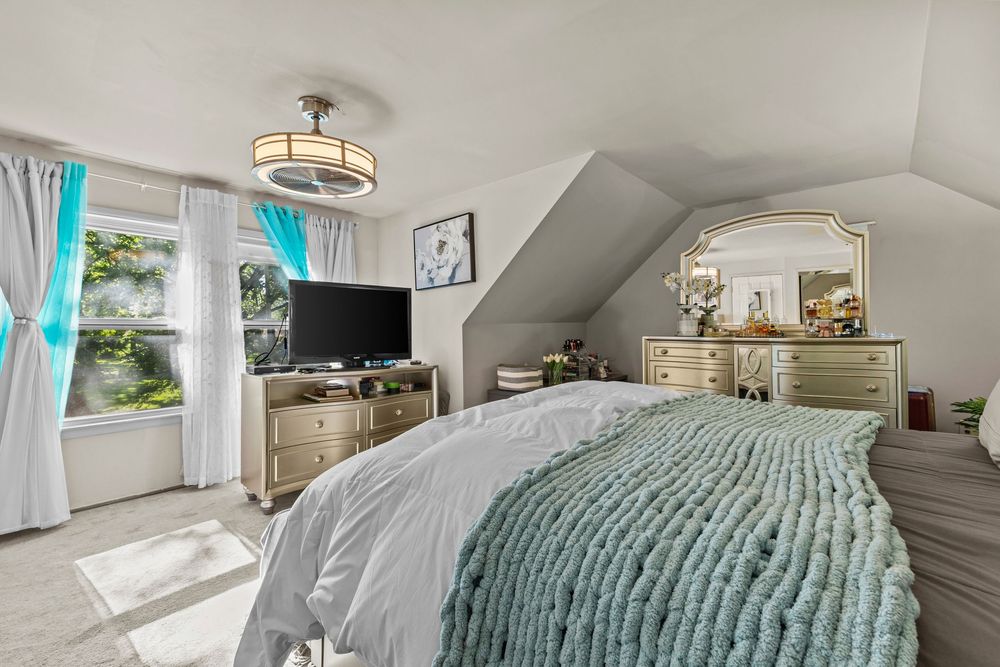 Bright attic bedroom with sloped ceilings, teal accents, gold dresser, and natural window light.