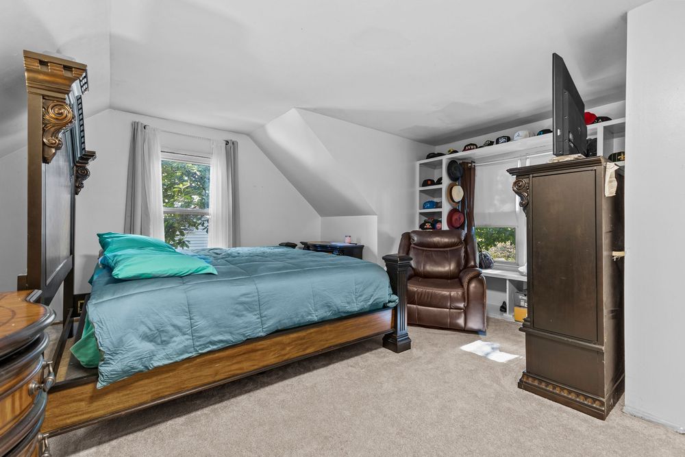 Carpeted bedroom with sloped ceiling, built-in shelves, and teal bedding.