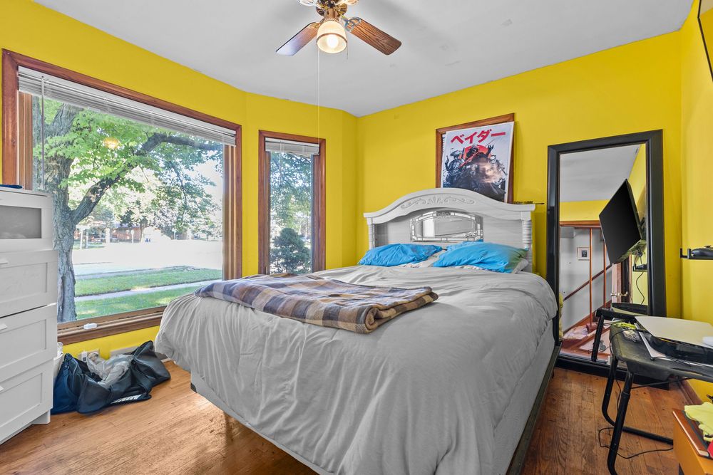 Bright yellow bedroom with large window, hardwood floors, and ceiling fan.