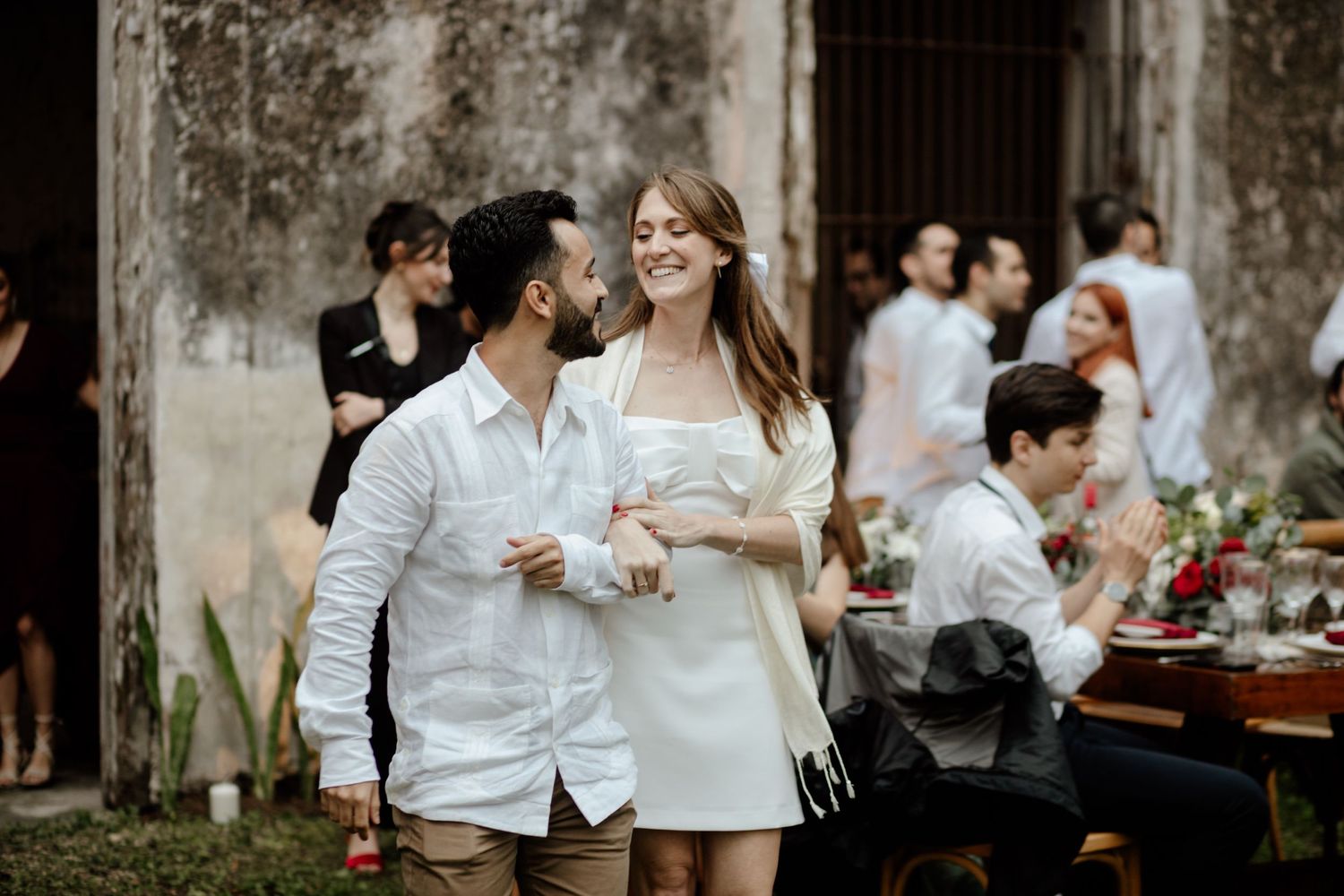 A couple enjoying drinks at an elegant outdoor garden party with rustic stone walls.
