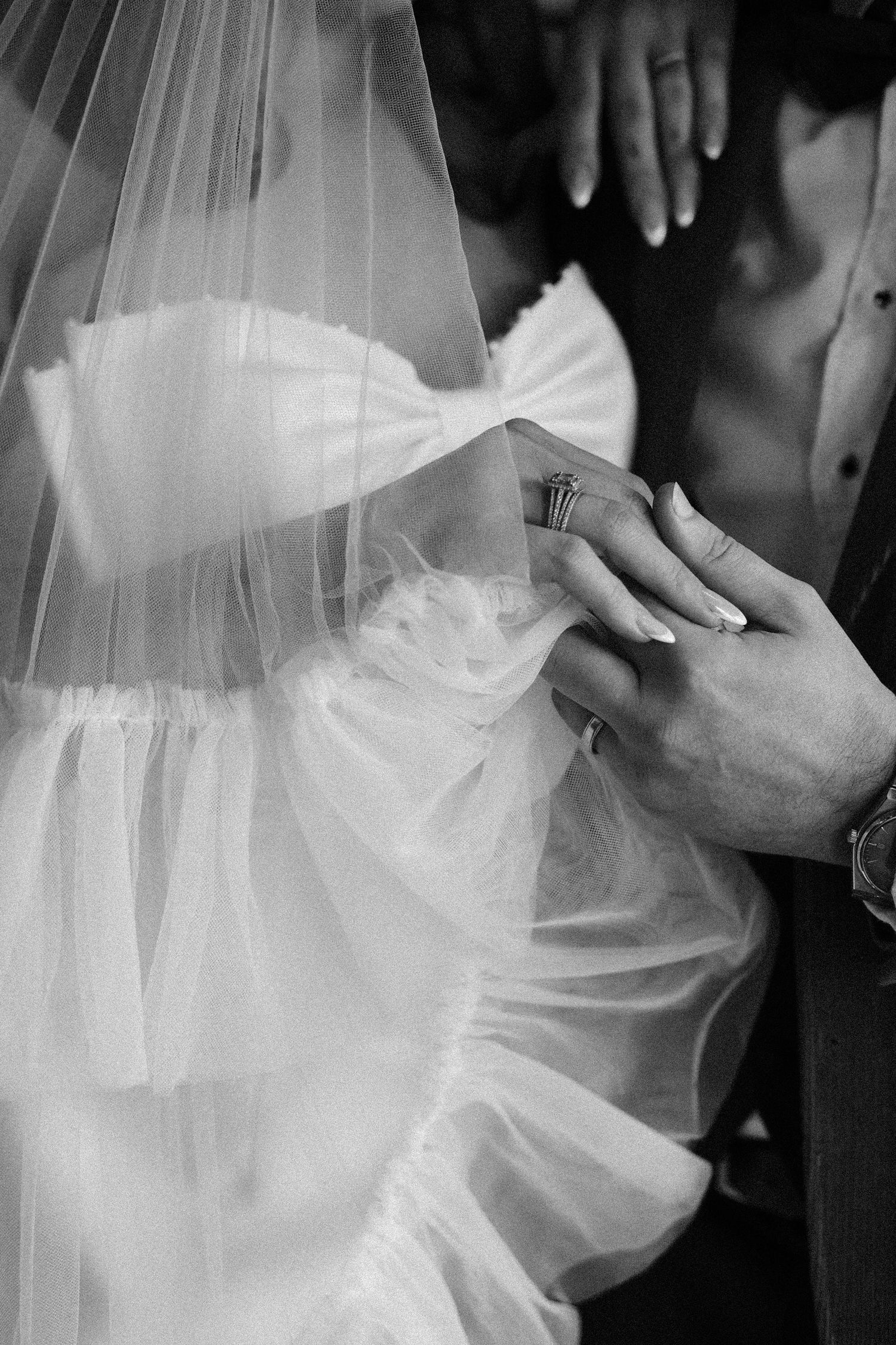 Close-up of hands during a wedding ring exchange, with flowing white veil in frame.