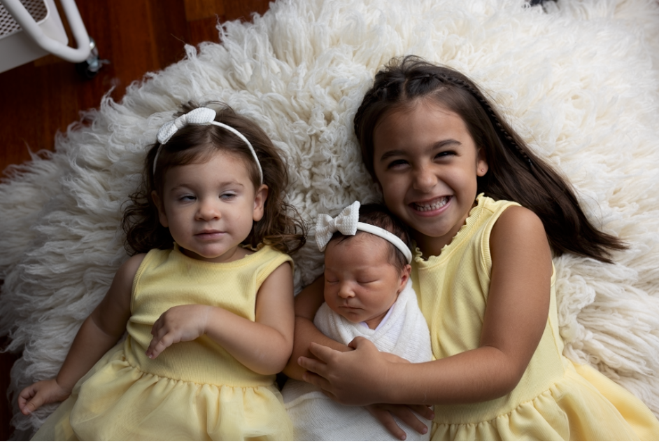 Three siblings wearing matching yellow dresses laying together on a white fluffy rug - straight out of camera and undedited